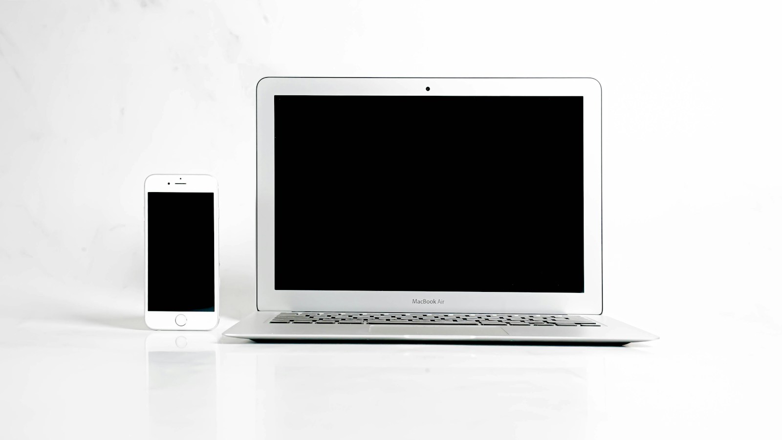 Teléfono móvil y computadora portátil con pantallas apagadas sobre una superficie blanca.